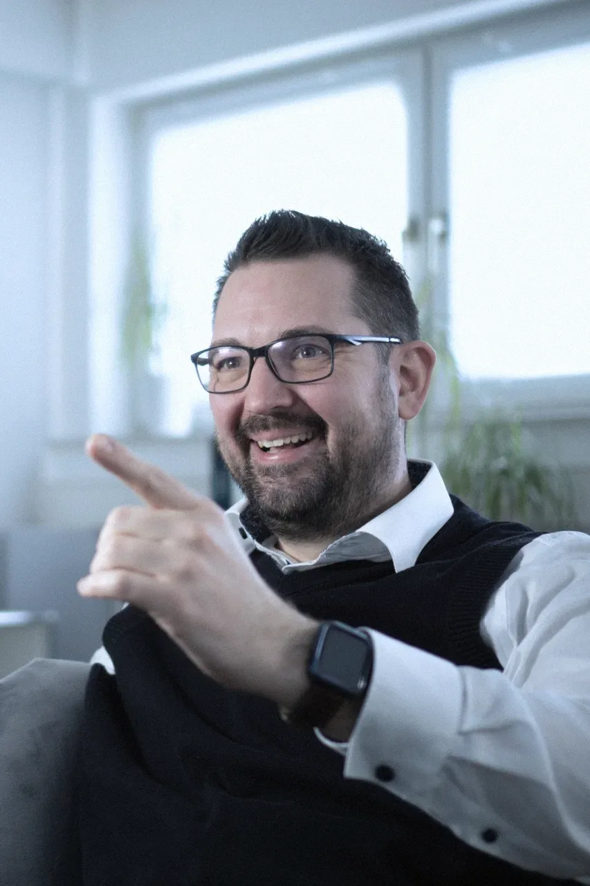 Robin Steinheimer lacht im Büro und zeigt mit dem Finger nach vorn